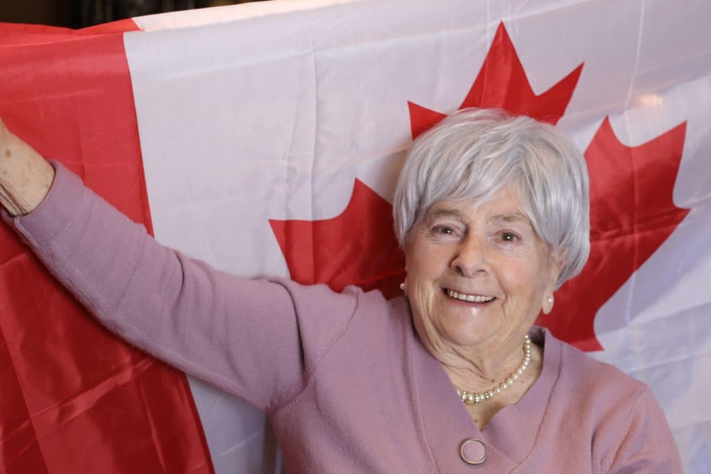 An older woman proudly holding a Canadian flag during a senior benefit event in Canada.