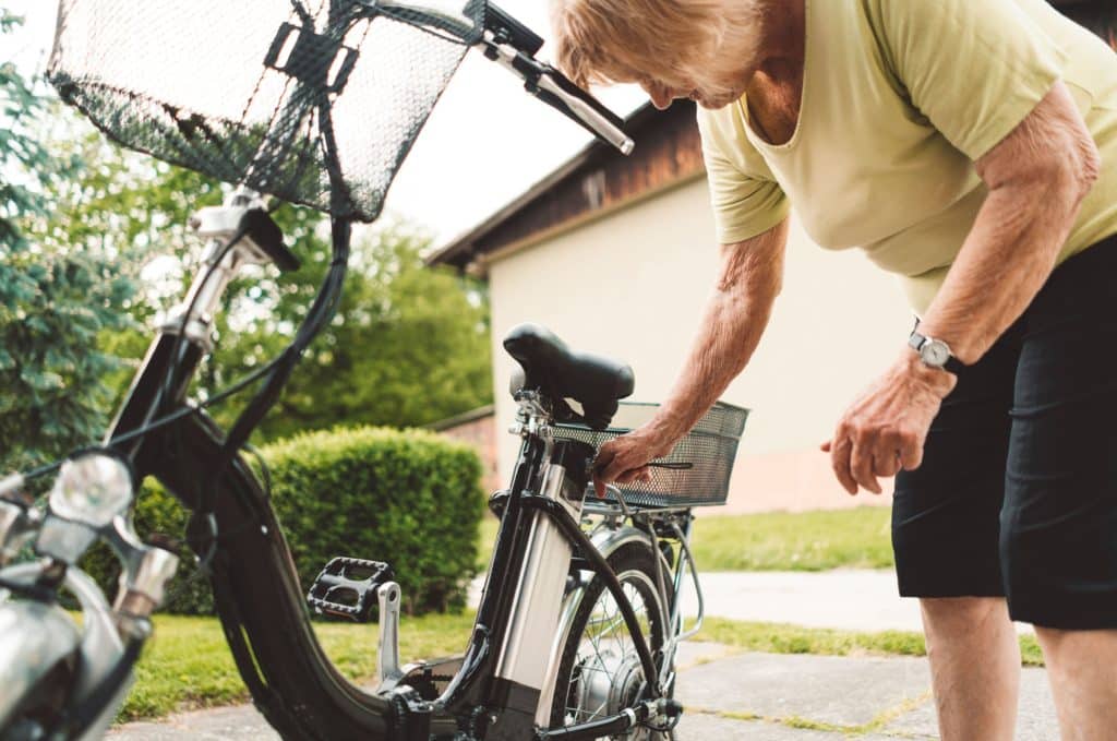 An elderly woman is using the best electric bike for seniors to put her bike on a bike rack.