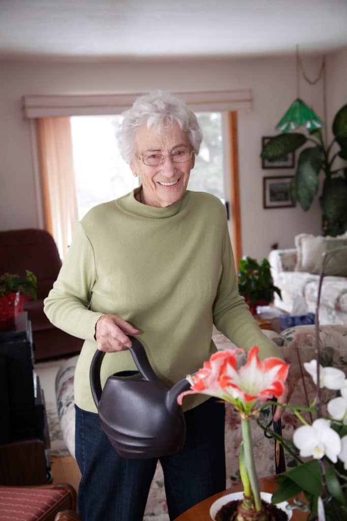 A senior woman using a watering can in an assisted living environment.