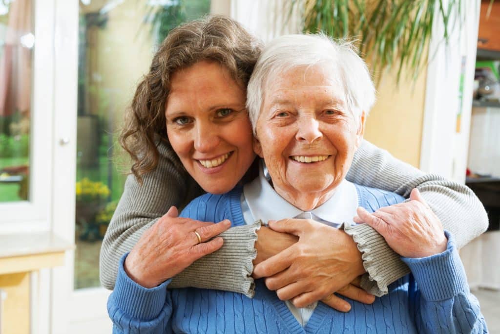 A woman embraces an elderly woman in the comfort of a home, supported by Jewish Family Services of Tucson for seniors.
