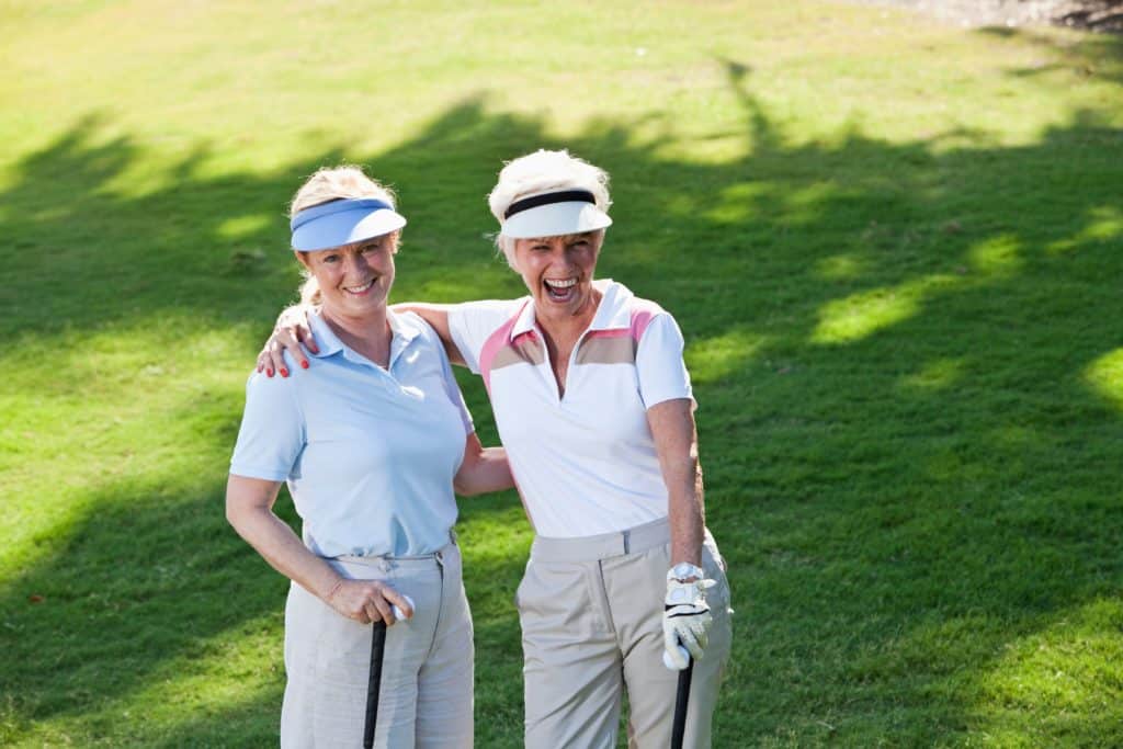 Two older women improve their golf swing on a course designed for seniors with limited flexibility.