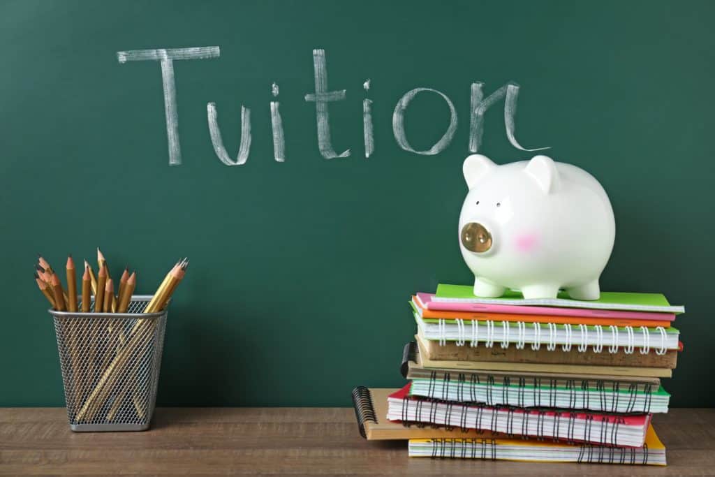 A piggy bank sits on top of a stack of books with the word tuition written on it, highlighting universities offering free tuition for seniors.