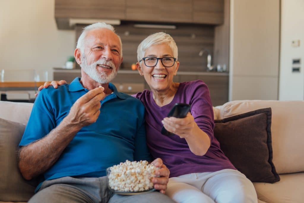 An older couple enjoying the top movies for seniors in 2023 while snacking on popcorn.