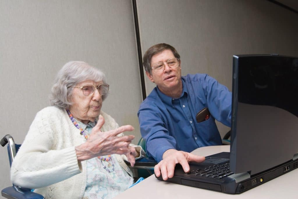 A man and a woman volunteer to help seniors with technology at a table with a laptop.